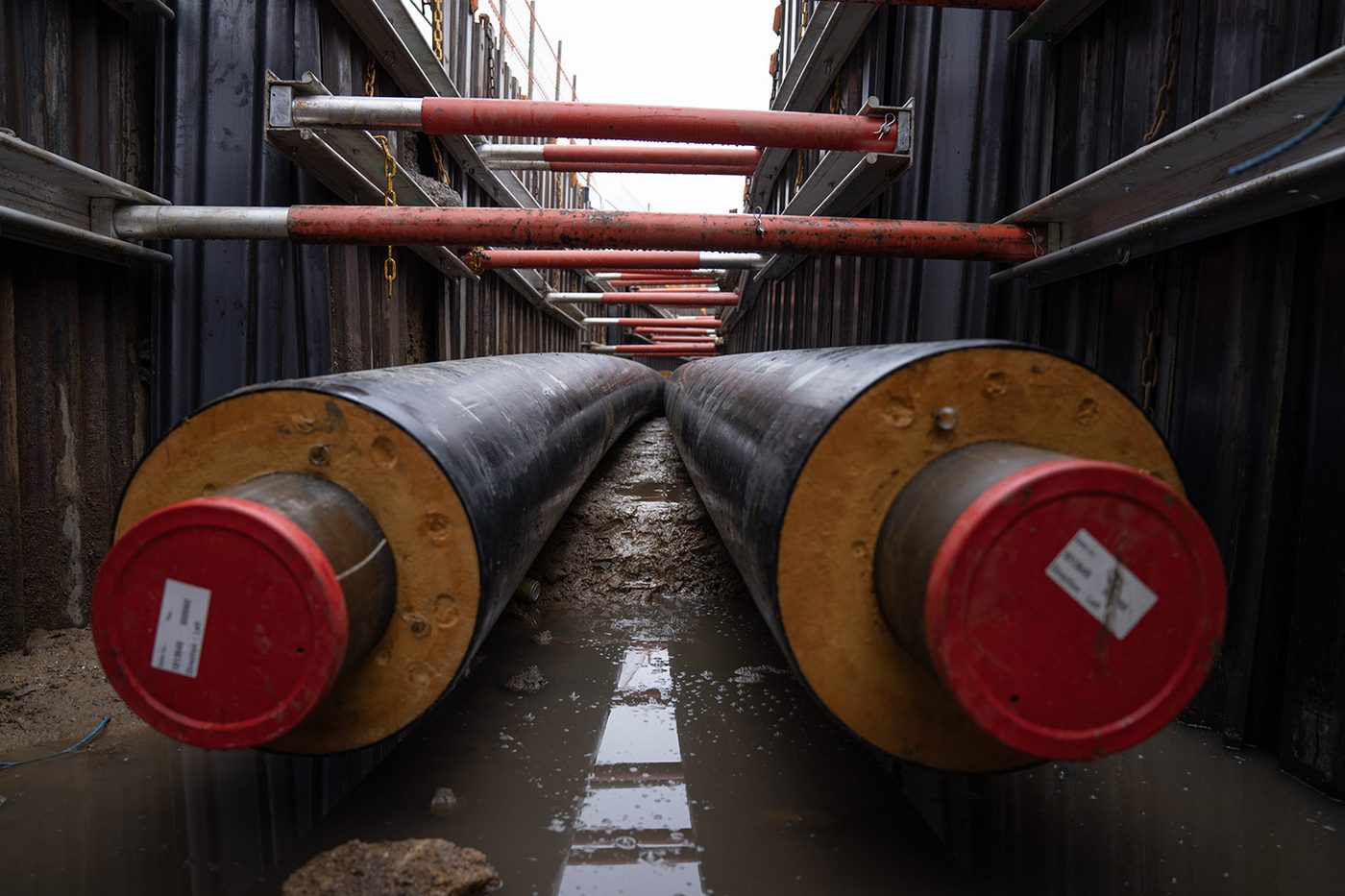 Two pre-insulated district heating pipes lying side by side in a shored trench, seen from the open ends.